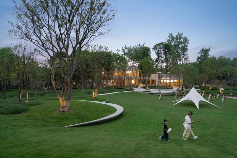 Curved pathways leading through lawn toward illuminated building at dusk with visitors strolling