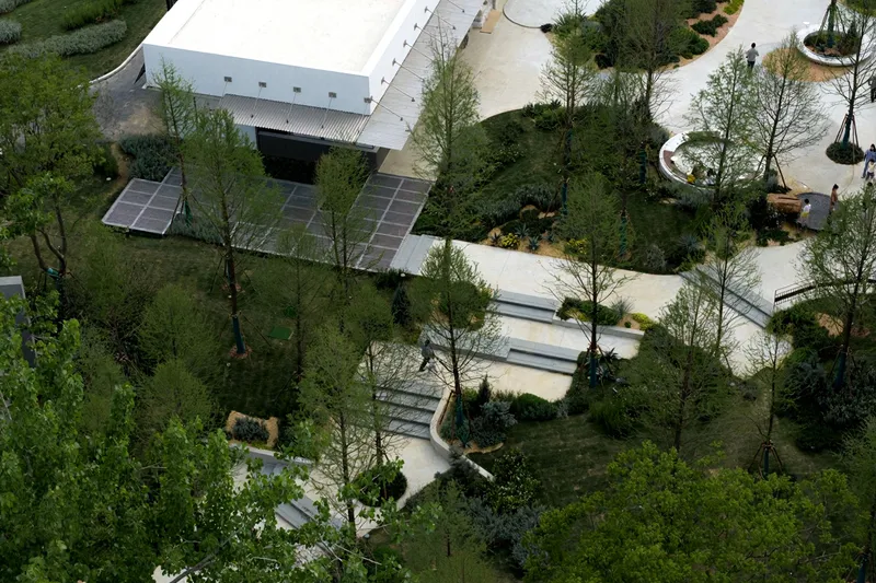 Aerial view of white pavilion with folded roof and concrete paths winding through planted berms
