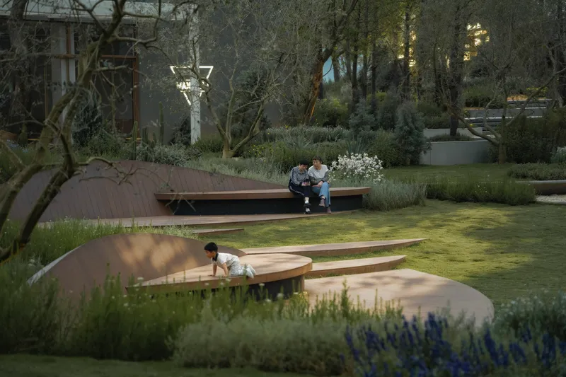 Circular timber seating platforms with children playing among planted beds and mature trees