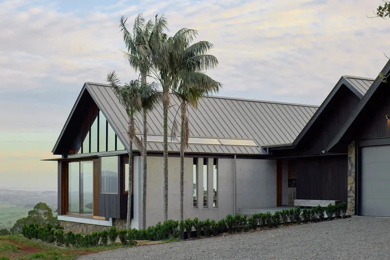 Entry facade with glazed gable and palm trees against a pale evening sky