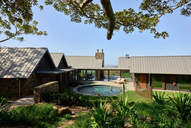 Courtyard with circular pool framed by pitched roofs and native plantings beneath a spreading tree