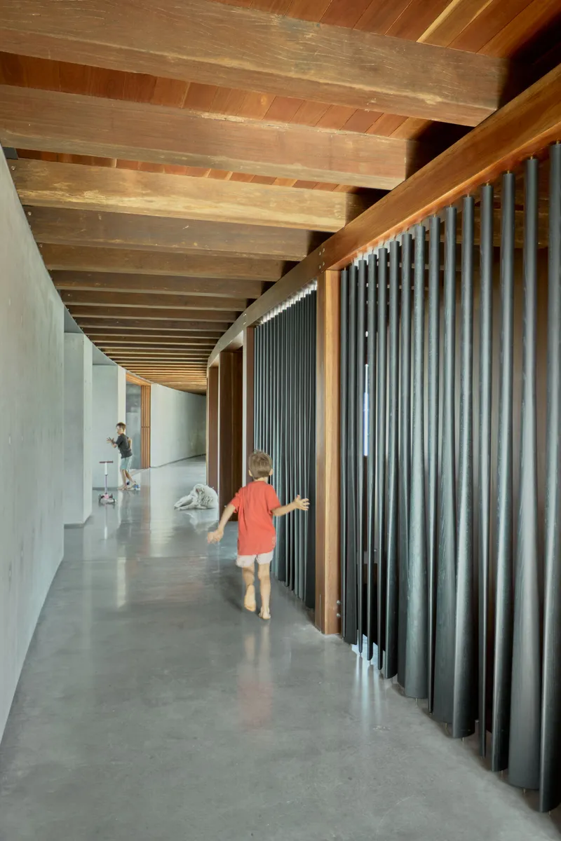Corridor with corrugated metal screen and timber ceiling beams as a child walks along polished concrete