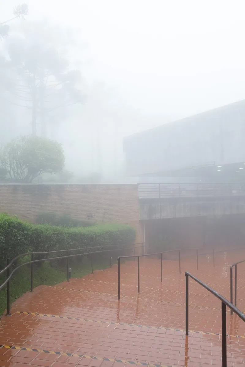 Brick staircase with metal railings descending through dense fog toward a courtyard and concrete walls