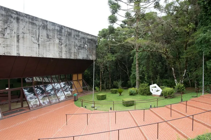 Cantilevered concrete volume above a glazed facade overlooking stepped brick terraces and a lawn with sculptures