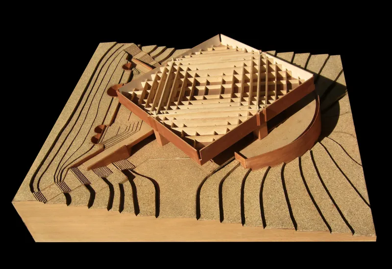 Physical model showing terraced landscape with timber-framed pavilion and curving wall under directional lighting