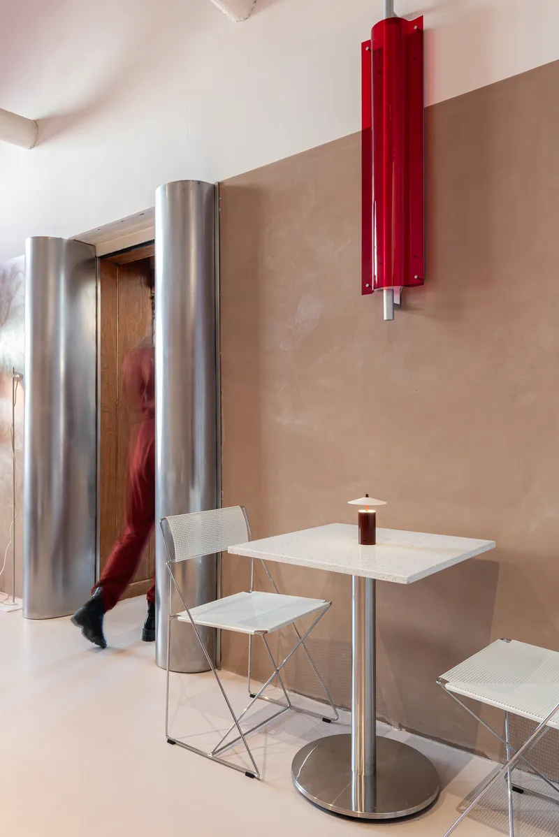 Interior seating area with cylindrical steel columns, a red wall-mounted radiator, and a person walking past