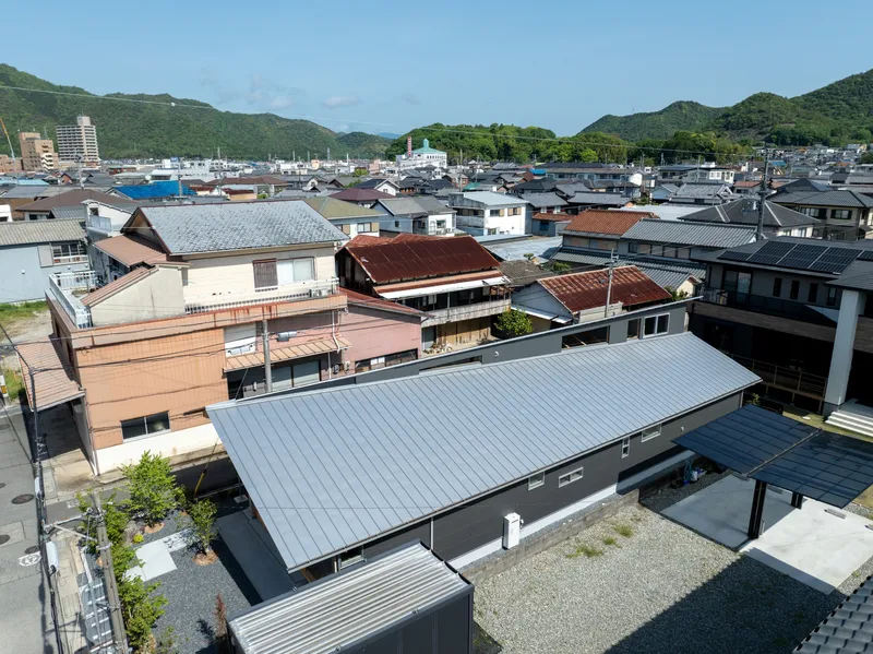Aerial view of the corrugated metal roof nestled among neighboring residences with mountains beyond