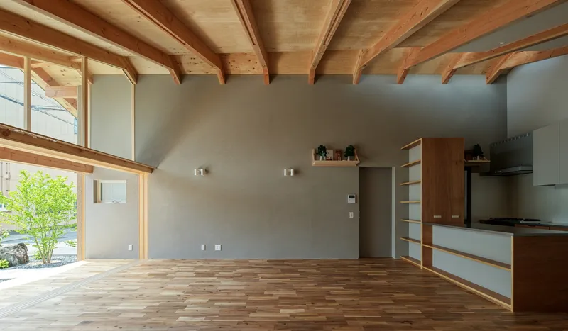 Open living space with exposed timber rafters, grey plaster walls, and timber and white kitchen cabinetry