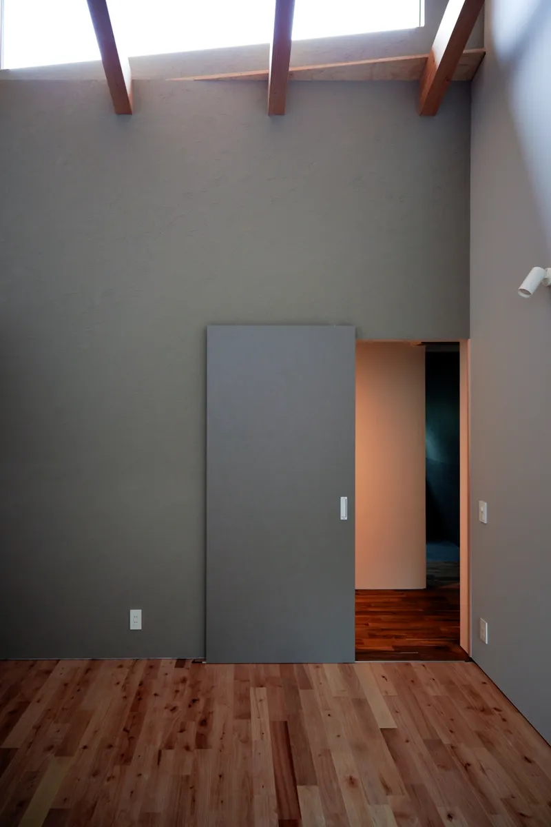 Flush grey sliding door opening to reveal a lit corridor beneath exposed timber ceiling beams