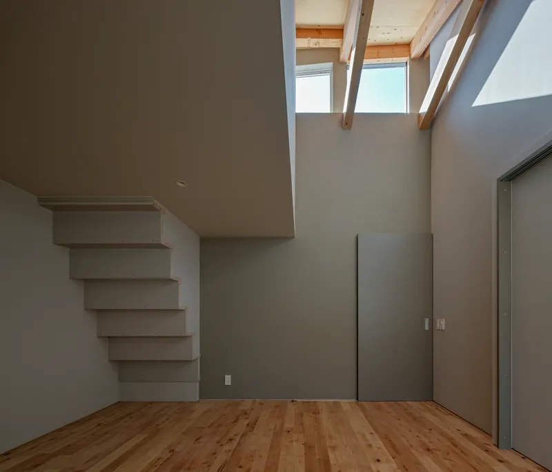 Second-floor room with floating white shelves, clerestory windows, and timber flooring at the ceiling edge