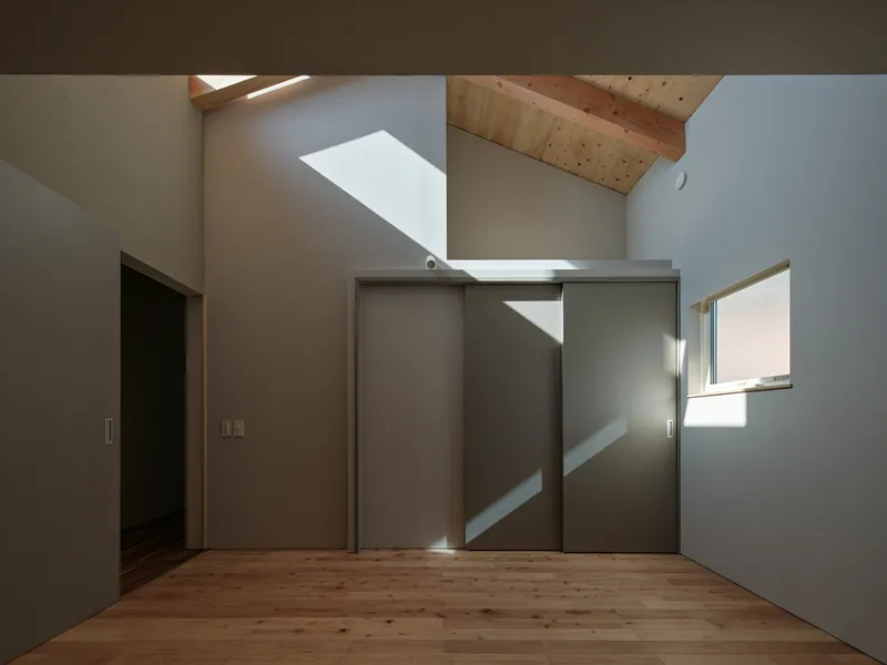 White-walled room with sliding closet doors and skylight casting angular shadows on the timber ceiling