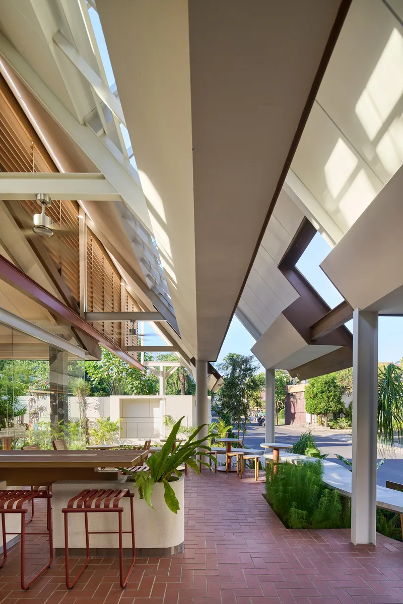 Covered outdoor terrace with herringbone brick floor and concrete columns opening to planted courtyard