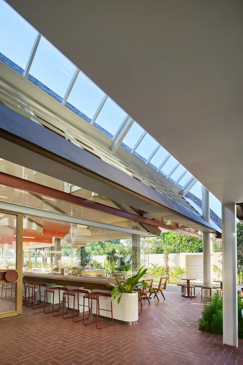 View through continuous clerestory glazing above terrace seating with outdoor brick paving and greenery