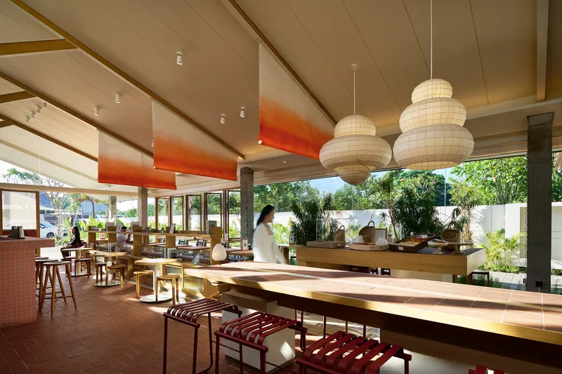 Dining area with long timber tables, globe pendant lights, and views to planted courtyard beyond