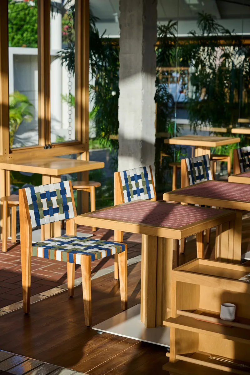 Timber dining chairs with woven striped seats beside concrete column in dappled shade