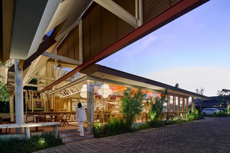 Covered entrance canopy with exposed timber beams and wood ceiling above planted beds at dusk