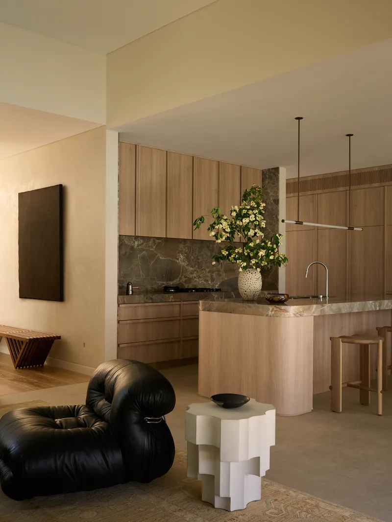 Living room view toward the kitchen island showing a black leather chair and white geometric side table