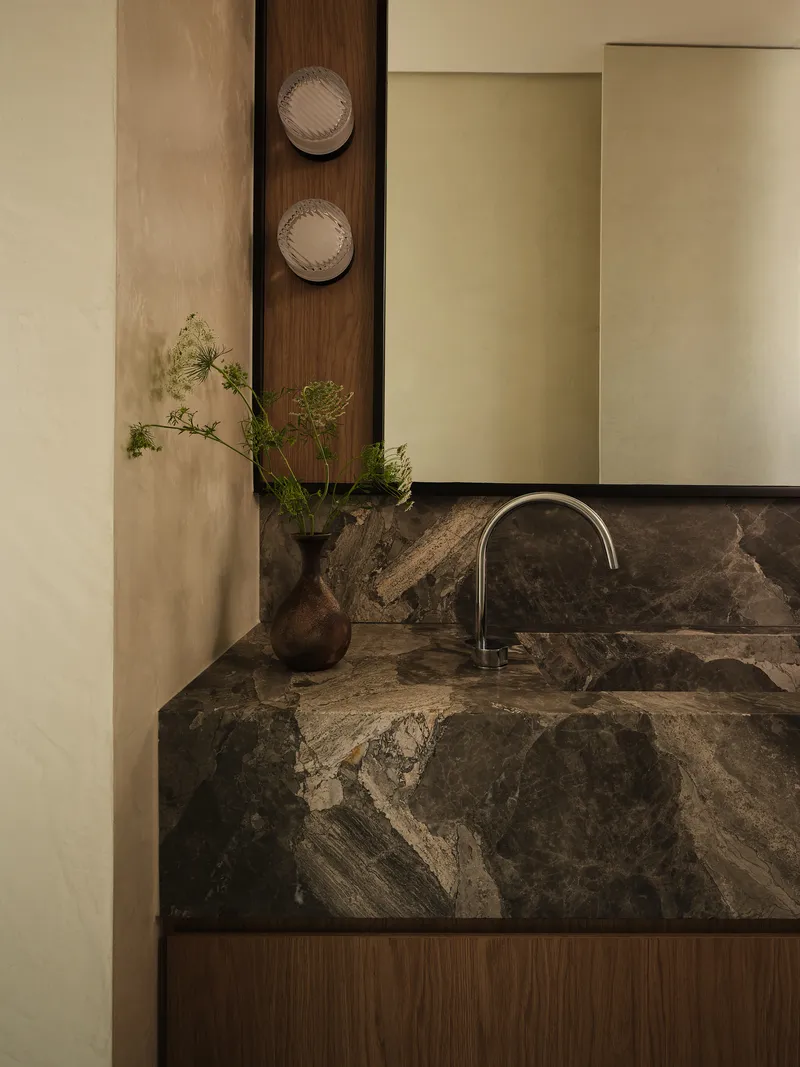 Bathroom vanity with dark veined stone countertop, integrated sink, and vase of green stems