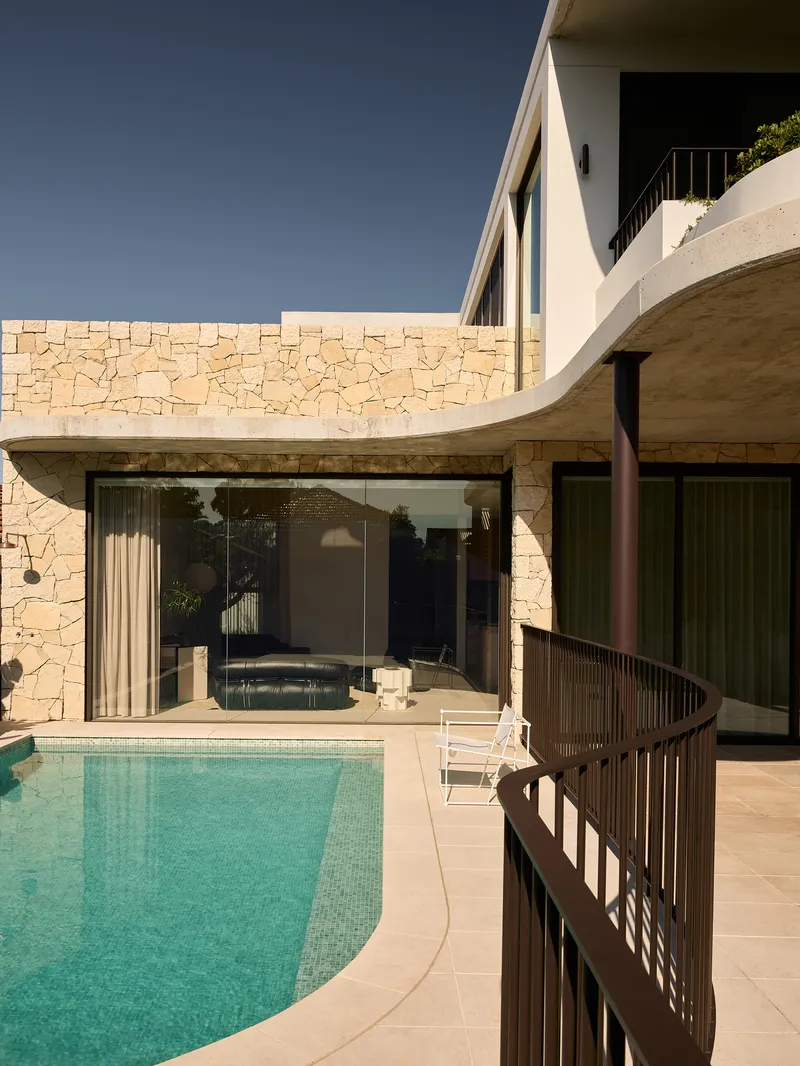 Pool terrace with curved stone wall and spiral balustrade beneath cantilevered upper floor