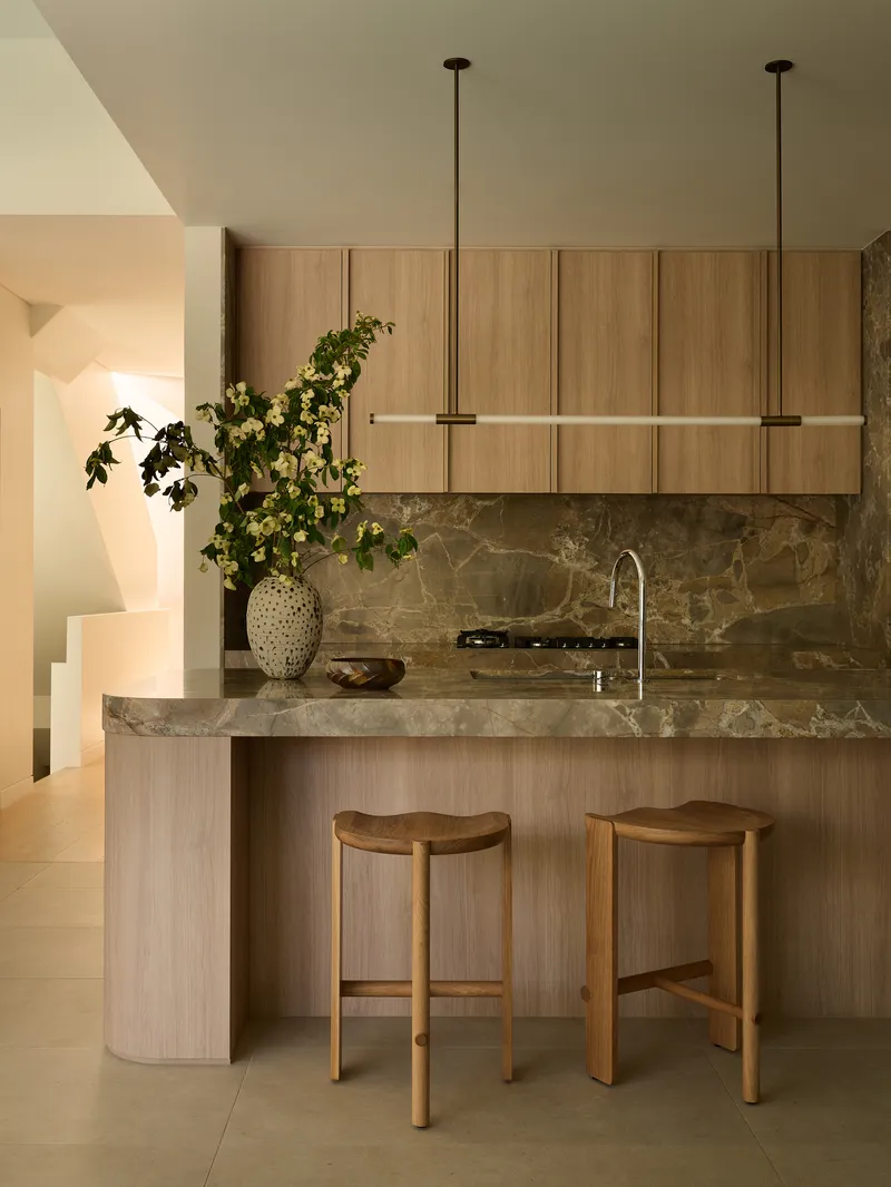 Kitchen island with grey marble countertop and timber cabinetry illuminated by pendant fixtures