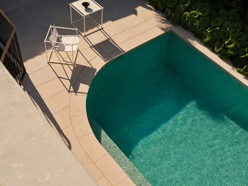 Overhead view of the curved pool with teal tile and limestone deck in midday sun