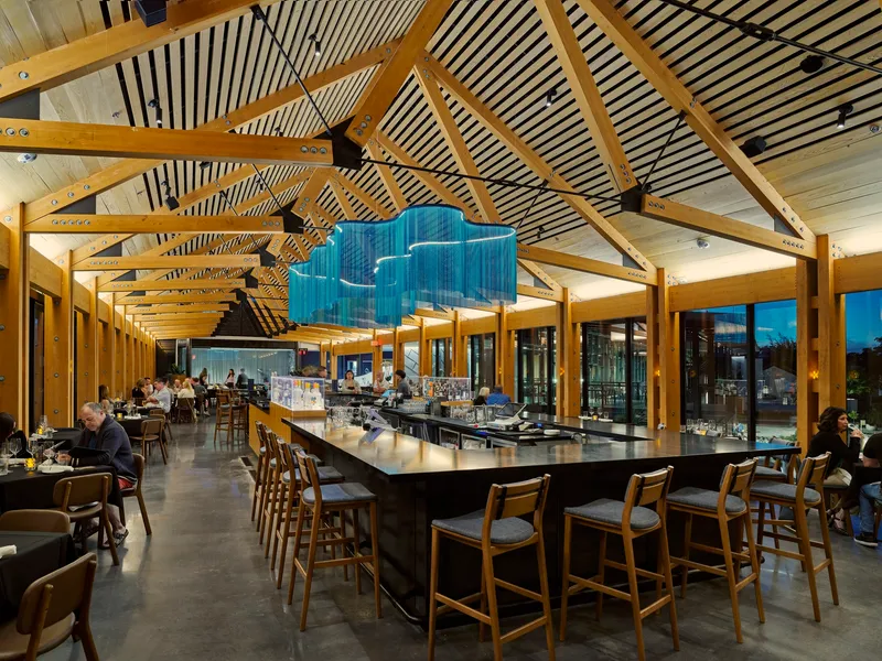 Interior dining space with exposed timber trusses and striped ceiling panels above a central bar counter