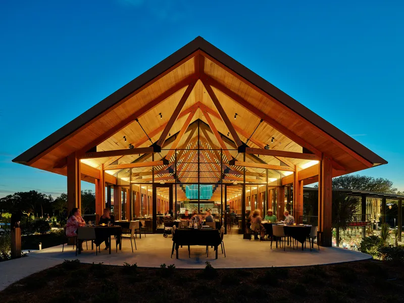 Open-air dining terrace beneath a timber gable roof with guests seated outdoors at dusk