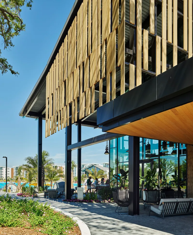 Covered terrace with steel columns and timber soffit beneath a cantilevered upper level clad in vertical slats