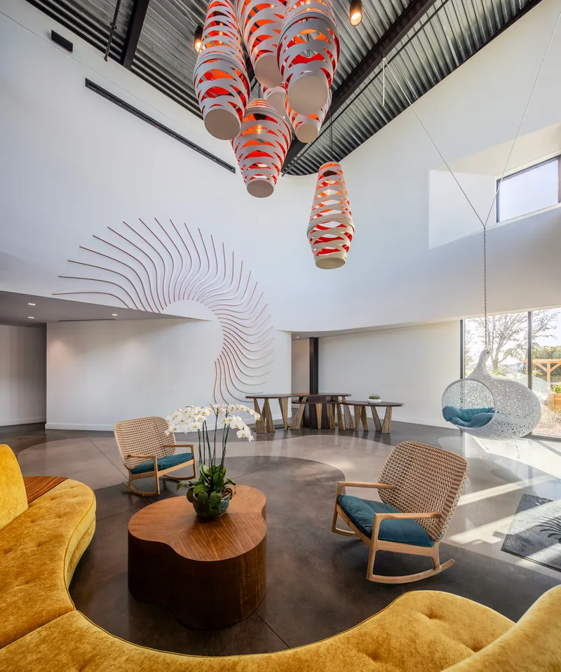 Double-height lobby with sculptural orange and white pendant lights hanging above a circular seating arrangement