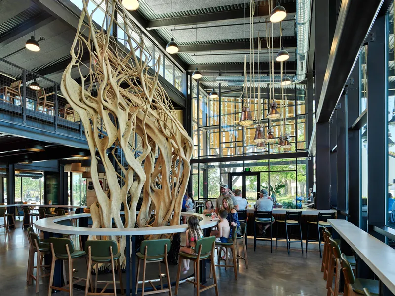 Sculptural driftwood installation rising through a circular bar counter surrounded by seated diners
