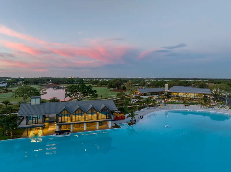 Aerial view of poolside pavilion with gabled roofs and lakeside golf course at dusk