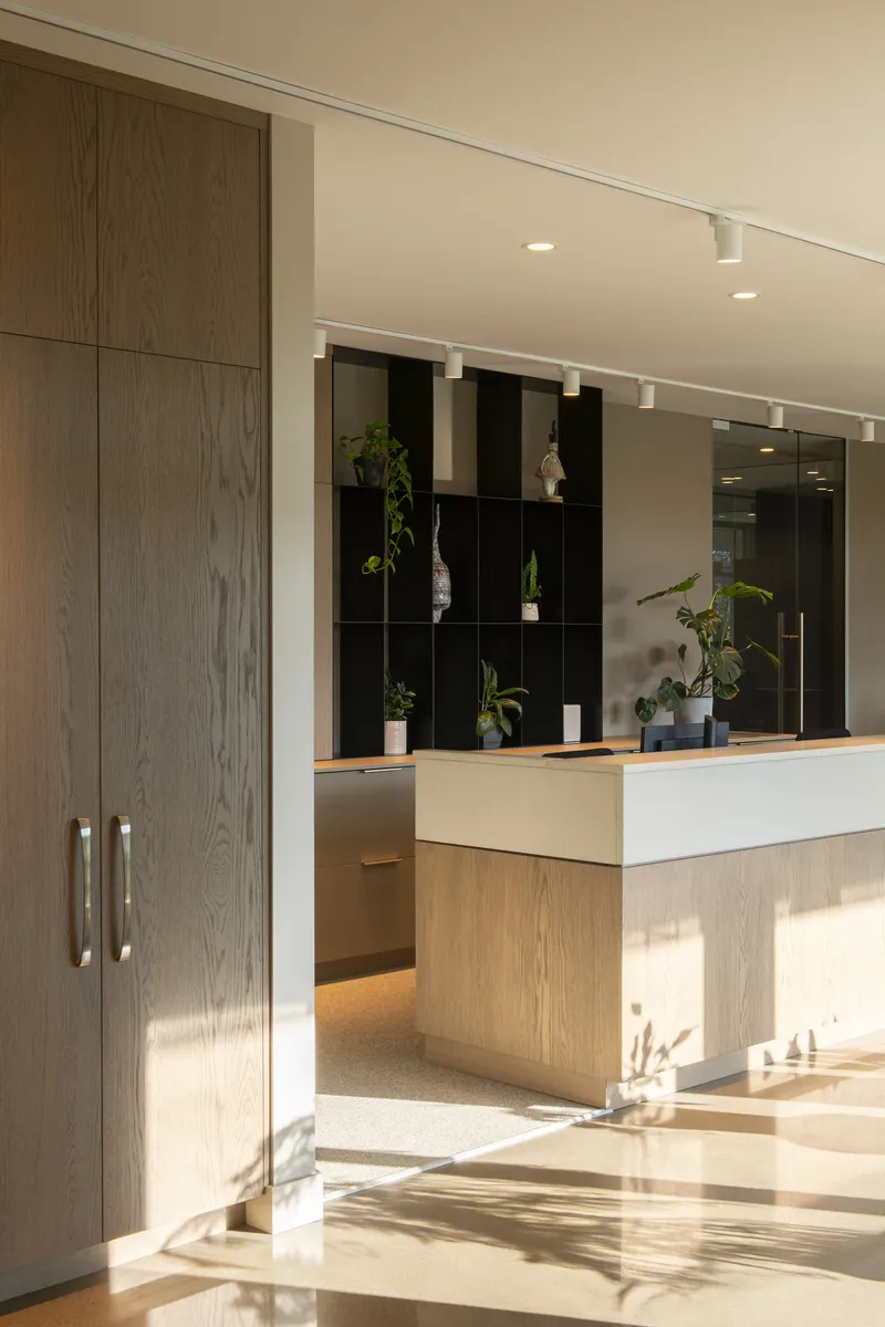 Reception desk with light oak millwork and black cubby shelving illuminated by afternoon sun