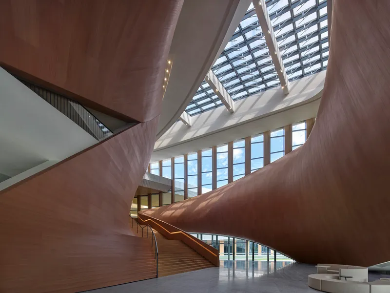 Interior atrium with timber-clad staircase rising beneath a geometric skylight with angular glazed openings