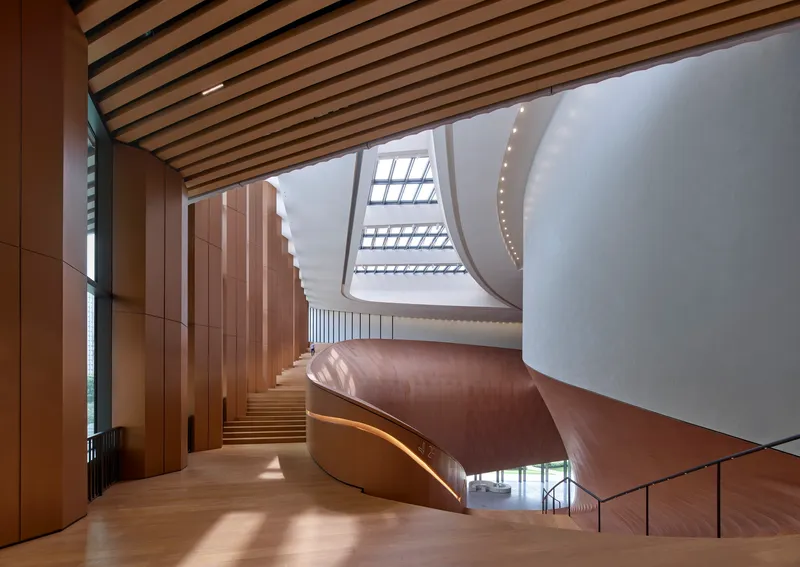 Interior view of the helical timber-clad staircase rising beneath a skylit atrium with timber batten ceiling