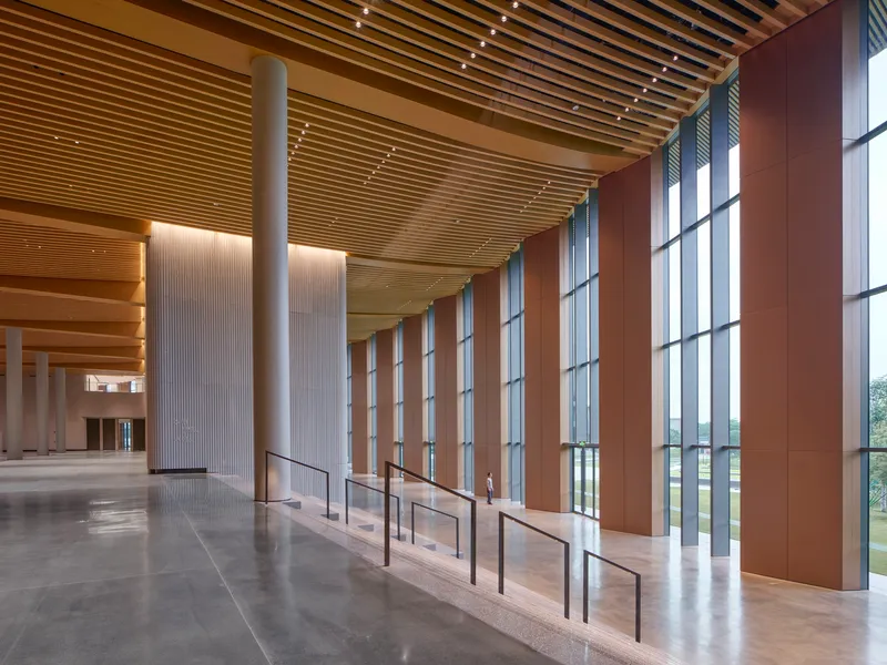 Interior lobby with tall glazed curtain wall filtered by timber screens and track lighting along timber slat ceiling