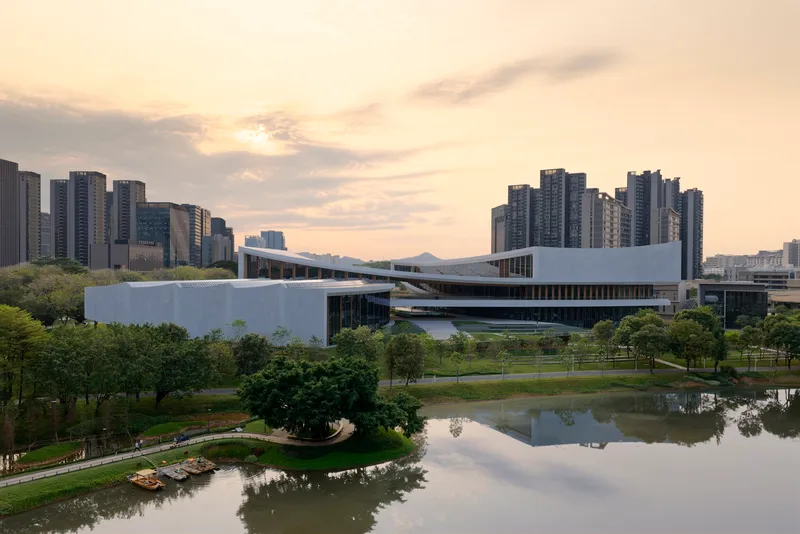 Aerial view of the white cultural center with layered rooflines beside a reflecting pond at dusk