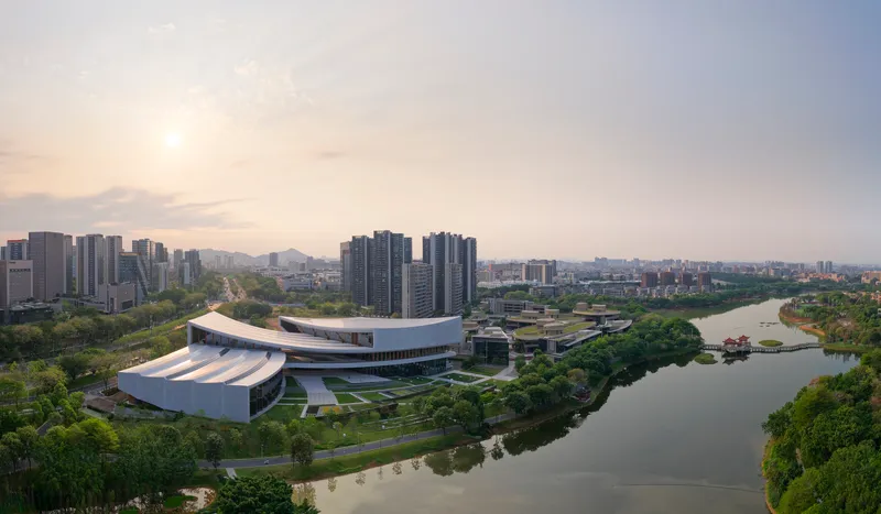 Wide view showing the curved volumes and horizontal louvers of the riverside complex at sunset