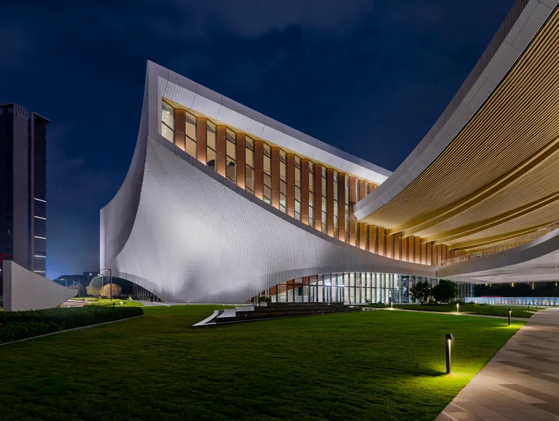 Curved white facade with vertical louvers rising above a grassy lawn at twilight