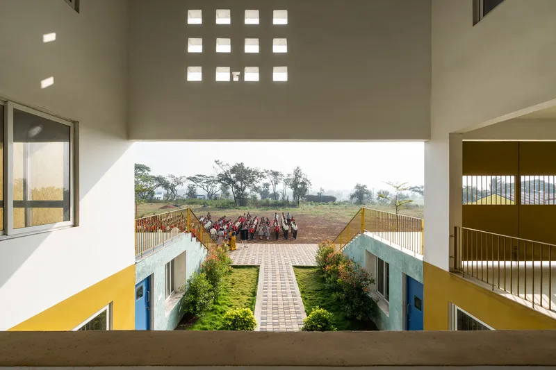 View through perforated wall opening toward courtyard with children assembled on the terrace below