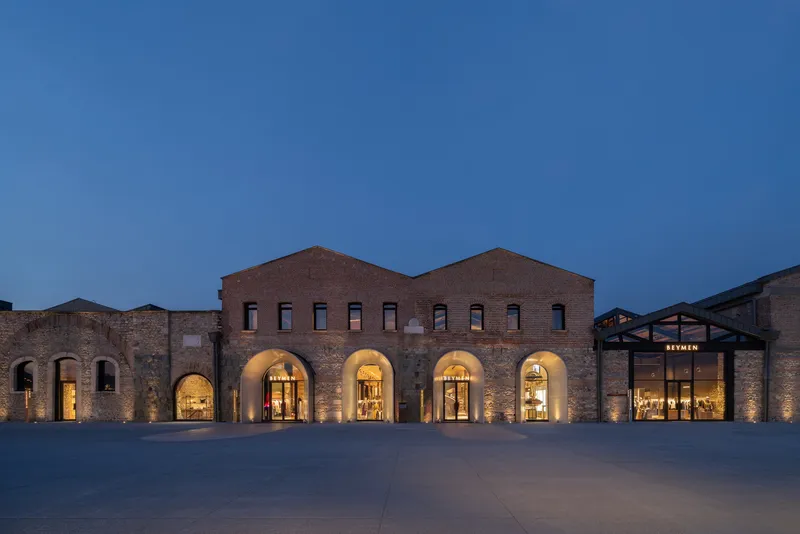 Restored brick warehouse facade with illuminated arched openings and central entry canopy at twilight