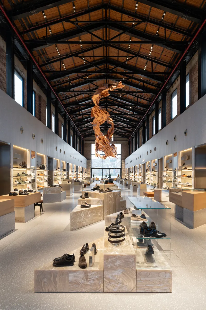 Interior retail hall with exposed timber trusses and a sculptural installation suspended above display tables