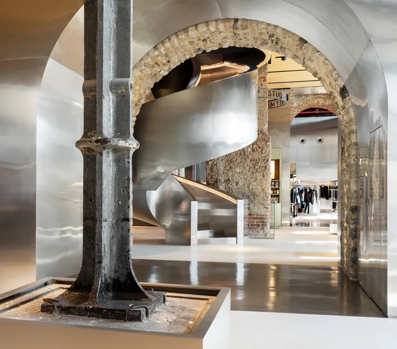 Polished steel spiral staircase framed by a preserved brick arch and cast iron column