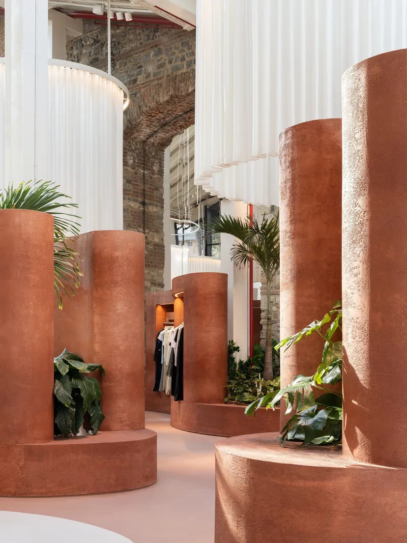 Terracotta cylindrical columns and planters with palms in a white curtain divided interior under exposed brick vaults