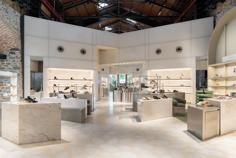 Retail floor with white display volumes and lit shelving beneath exposed timber ceiling and industrial steel trusses