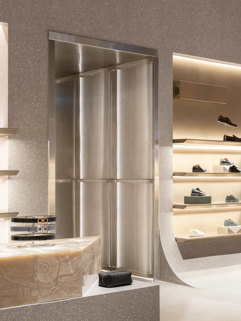 Brushed stainless steel elevator door flanked by terrazzo walls and curved white display shelves with shoes