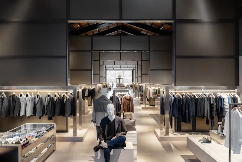 Symmetrical view through clothing racks toward nested portal frames and exposed timber roof trusses with mannequin in foreground
