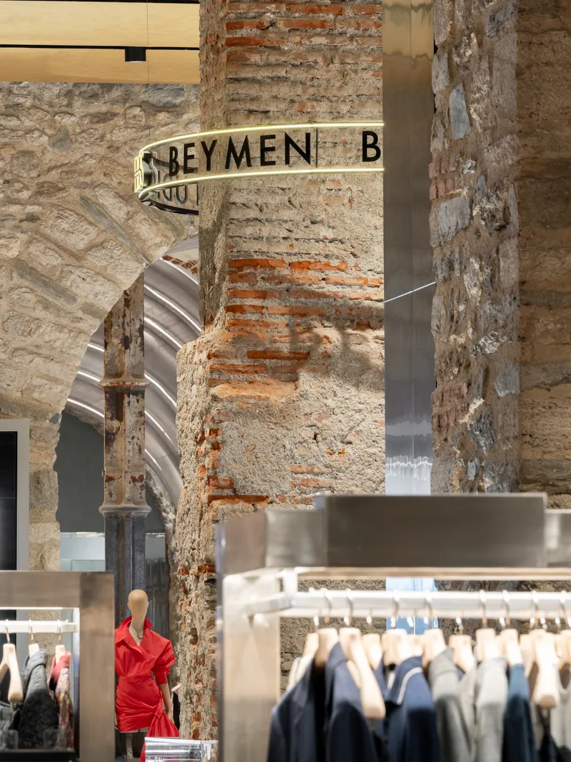 Weathered masonry columns with remnant signage next to brushed metal display fixtures and clothing racks