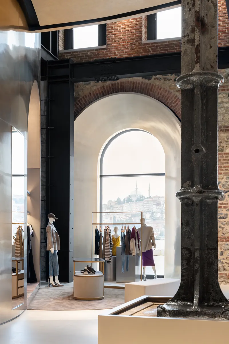 Retail interior with exposed brick arch, weathered column, and arched window framing a distant hillside view