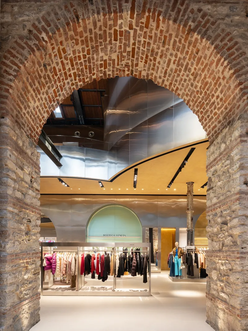 View through exposed brick vault showing reflective sculptural ceiling and retail displays on ground floor below