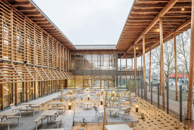 Covered courtyard with exposed timber joists and horizontal wood slat screens surrounding scattered seating at dusk